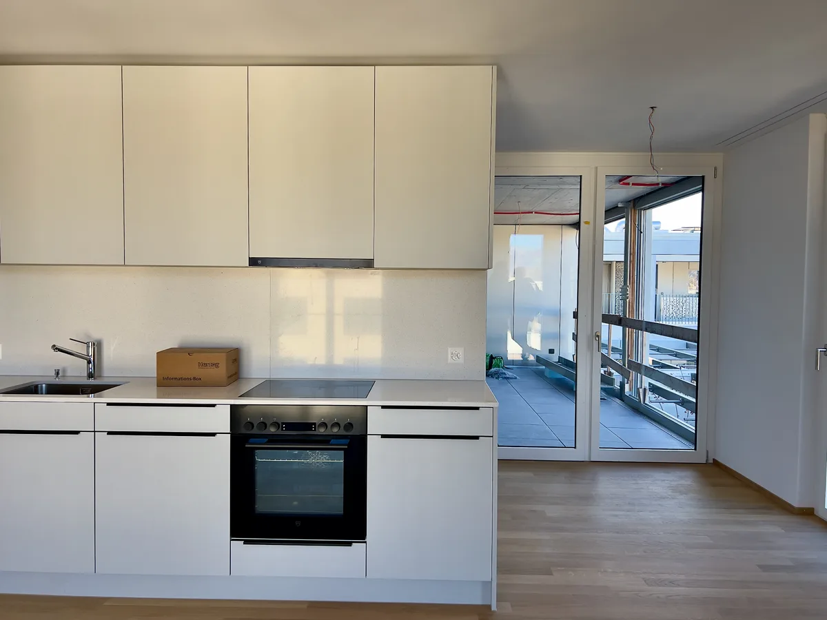 Im Vordergrund ist zur Hälfte eine Küchenzeile einer Wohnung zu sehen, rechts daran vorbei ist die Sicht auf den Balkon frei.